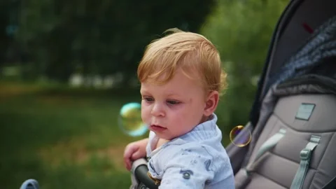 Blonde-haired child in stroller gazes at floating bubbles Stock Footage 340885915