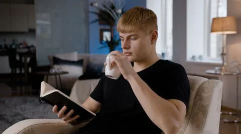 Blonde-Haired Young Man Drinking Coffee and Reading in Cozy Room Stock Photos