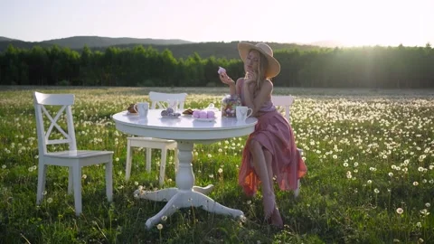 A blonde in a hat poses in front of the camera sitting at a table. Morning tea Stock Footage 256155275