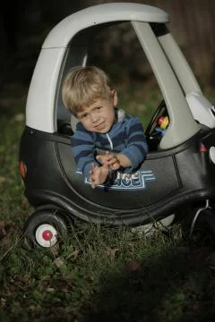 Blonde Little boy driving big toy police car outdoors Stock Photos