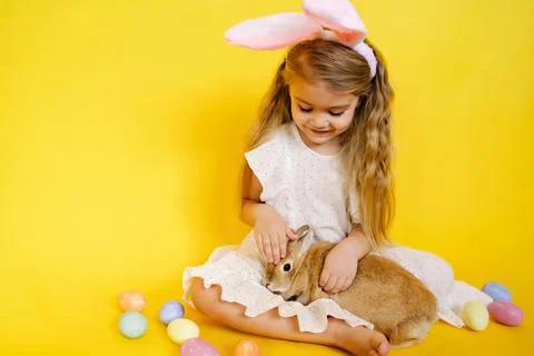 Blonde little girl with bunny ears holding easter bunny in her arms on yellow Stock Photos
