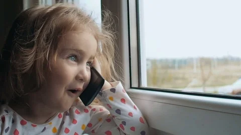 Blonde little girl talking on the phone. Sitting on the window sill. The chil Stock Footage