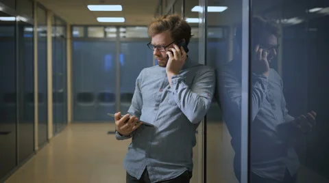 Blonde man in office building talking on the phone and simultaneously scans news Stock Footage 68622295