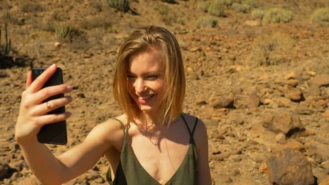 Blonde Model Taking a Selfie with Dry Rocks and Lands in the Background Video stock 114175334