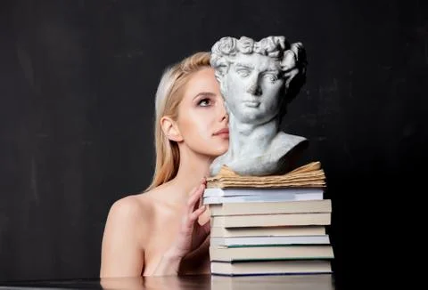 Blonde next to an antique bust of a man on books Stock Photos