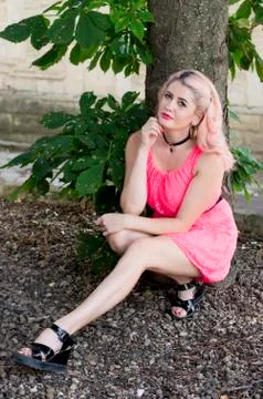 Blonde in pink sat down by the tree Foto stock