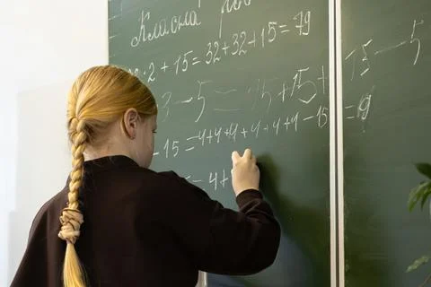 A blonde schoolchild writes complex math equations on a green chalkboard in.. Stockfoto's
