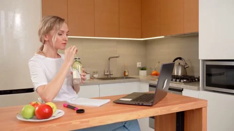 The blonde is sitting at the table in the kitchen, drinking lemonade from a Stock Footage 153040659