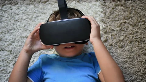 Blonde small boy lying on the carpet showing like and putting on VR headset Stock Footage 250364090