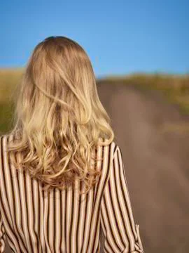 The blonde is walking along a country road in a striped dress from the back Stock Photos