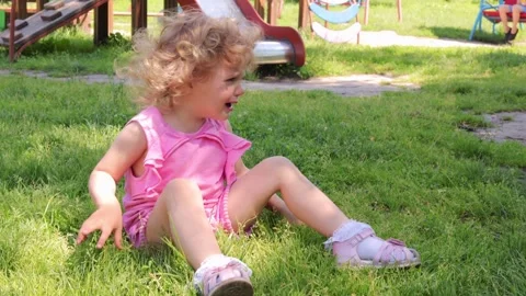 Blonde wavy haired sad upset little girl wearing pink dress sitting on grass on 動画素材 291406258