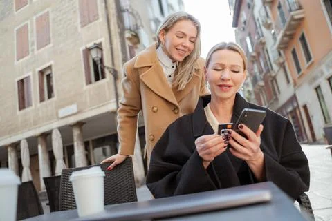 Blonde woman changing a sim card in her ohone, her freind helping Stock Photos