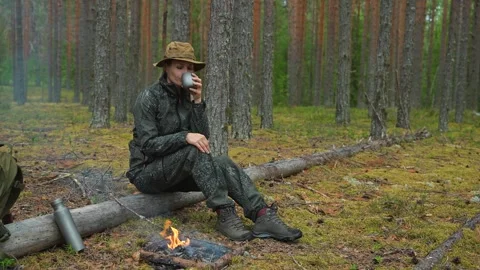 A blonde woman drinks tea while sitting by a forest campfire. A female traveler Video stock 315220899