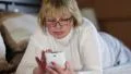 Blonde woman in glasses with white smartphone lying on the bed HD Footage