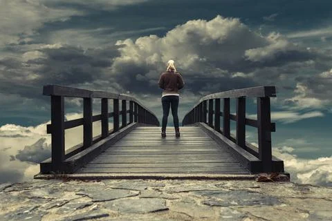 Blonde woman in jeans and jacket standing on a wooden bridge walking into clouds Stock Photos