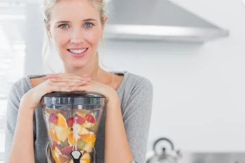 Blonde woman leaning on her juicer and smiling at camera Stock Photos