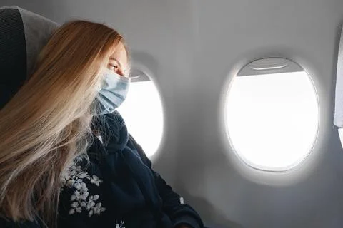 Blonde woman in medical mask sitting in the plane by the window Stock Photos