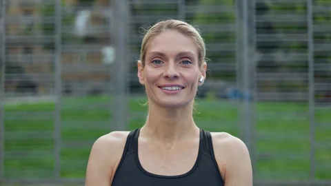 Blonde woman putting on earphone while standing on court and smiling at camera Stock Footage 252201921