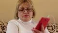 Blonde woman with red smartphone sits on the sofa and listens to music HD Footage