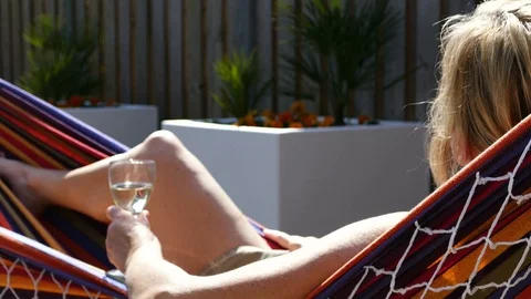 Blonde woman relaxes in a hammock enjoying a glass of wine Stock Footage