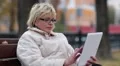 Blonde woman sits on the bench near the road and uses Tablet PC HD Footage