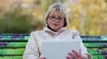 Blonde woman sits on the bench in public garden and uses white tablet computer HD Footage