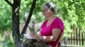 Blonde woman sits on the chair in garden and uses tablet computer HD Footage