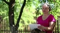 Blonde woman sits on the chair in garden and uses tablet computer HD Footage