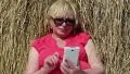 Blonde woman sits near haystack and uses smartphone HD Footage