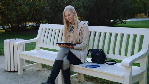 Blonde Woman Smiling Using Tablet Sitting on White Bench in Park Video stock 340739562