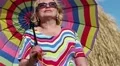 Blonde woman in sun glasses with many-coloured umbrella stands near haystack HD Footage