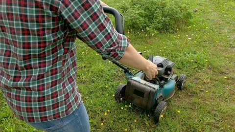 Blonde woman trying to start engine of a lawnmower, summer work in garden Stock Footage 119176516
