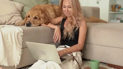 Blonde woman is using laptop, computer and working with dog at home Stock Footage 199191361