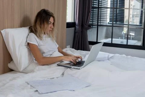 Blonde woman working on a computer while sitting in bed, urgent work on holidays Stock Photos