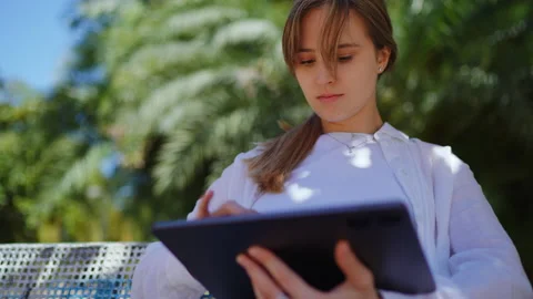 Blonde woman working on tablet while sitting on park bench, surrounded by Stock Footage 308388743