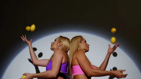 Blondes juggle lemons, standing with their backs to each other, slow motion. Stock Footage 199254026