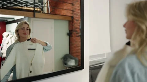 Blondy chooses clothes in the wardrobe at home. A woman tries on a white jacket Stock-Footage 234963853