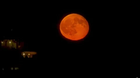 Blood full moon glowing brightly in dark night sky over city buildings Vídeo Stock 344751641