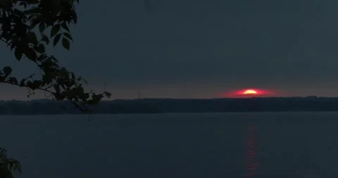 Blood-red sun setting over dark lake horizon, reflected on water at dusk Stock Footage 320019798