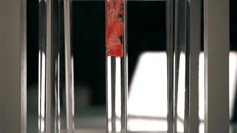 Blood slowly dissolves in a test tube with clear fluid. Slow motion Stock Footage 188749732