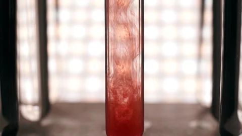 Blood slowly dissolves in a test tube with clear fluid. Slow motion Stock Footage 188750089