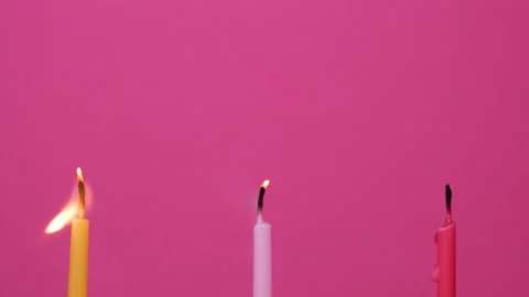 Blowing out Three cake candles burning on a pink background. Close up on yellow Stock Footage 161994591