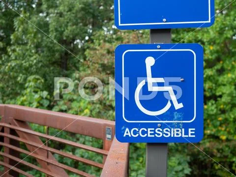 Blue accessible handicap sign hanging on nature hiking path Stock Photos