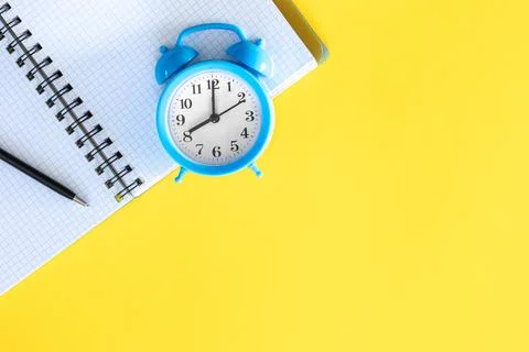 Blue alarm clock and notepad on a yellow background, flat design. Stock Photos