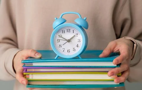 Blue alarm clock and stack of books in hands background, education Concept Stock Photos