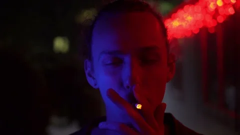 Blue and red light on young smoking man outdoors at night 库存影片 95861952