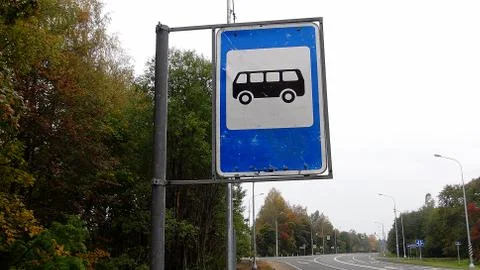 Blue and white bus stop sign on sky and trees background Stock Photos