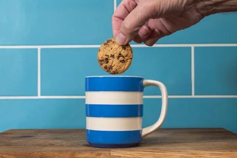 Blue and white cup of tea with a hand dunking a chocolate chip biscuit cookie 库存照片