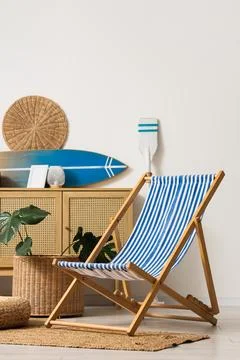 Blue and white striped deck chair in a beach-themed room with a surfboard and Stock Photos