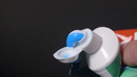 Blue and White Toothpaste Emerging from Tube on Dark Surface Video stock 336674413